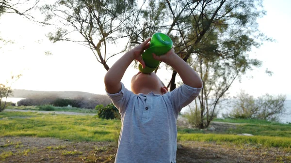 Adorabile bambino che beve acqua nel parco durante il tramonto — Foto Stock