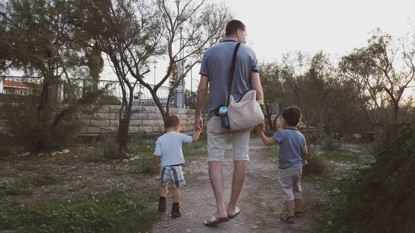 Vista trasera del padre con dos hijos pequeños caminando por el camino en el parque —  Fotos de Stock