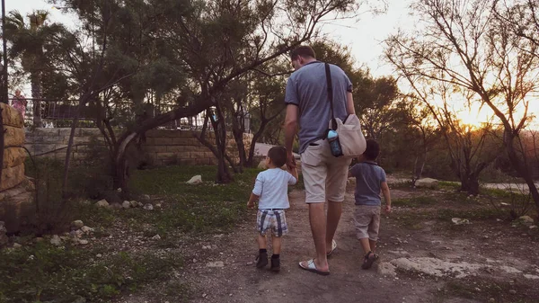 Back view of father with two young sons walking on the path in the park