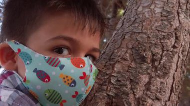 Yüz maskesi takmış anaokulu çocuğu ağaca tırmanıp sarılıyor. Ağır çekimde çekimleri kapat.