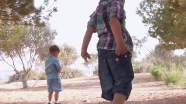 Kardeşler doğada oynuyor. Güneşli yaz gününde kirli ve kuru çimenleri keşfederek kayaları fırlatıyor.