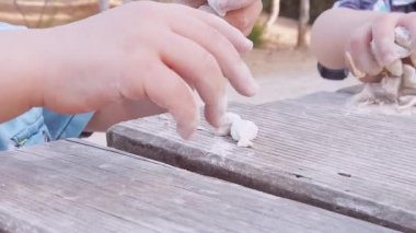 Beyaz çakıl taşlarıyla oynayan çocuklar. Yeni yürümeye başlayan çocuğun elini sıkın. Kardeşim arkada.