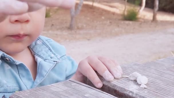 Anak berusia 3 tahun yang lucu bermain dengan kerikil di meja kayu di luar ruangan. Tutup tembakan di kepala — Stok Video
