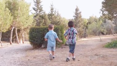 Sevimli anaokulu öğrencileri, kardeşler, el ele tutuşup parkta yürüyorlar. Yürüyen çocuk çöp kutusunu kontrol etmek için kaçıyor.