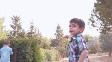Parkta oynayan sevimli kardeşler. Yaşlı olan, tahta çöp kutusuna bakan bir çocuğu işaret ediyor.
