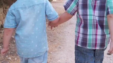 Sevimli kardeşler, el ele tutuşup parkta yürüyen iki anaokulu çocuğu. Arka plan yavaş çekim