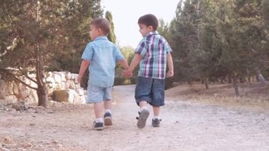 Sevimli çocuklar, kardeşler iki anaokulu çocuğu el ele tutuşup parkta yürüyorlar. Arka plan yavaş çekim