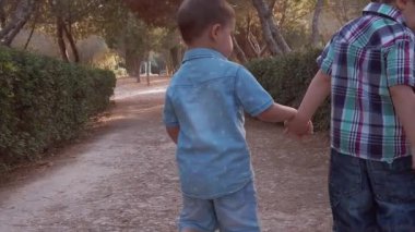 Sevimli kardeşler, el ele tutuşup parkta yürüyen iki anaokulu çocuğu. Arka plan yavaş çekim