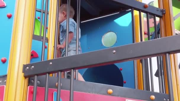 The little boy walks alone on the upper level of the climber on the playground — Stock Video