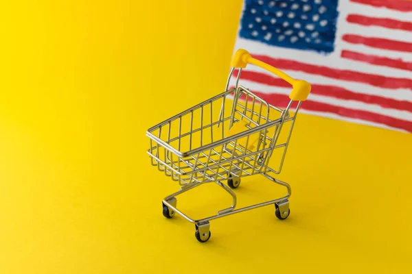 Mini market alışveriş arabası ve soyut el yazısı sarı arka planda Amerikan bayrağı. İthalat ve ihracat konsepti. E-ticaret. Amerikan yemek dağıtım servisi. Tatil indirimi ve online alışveriş.