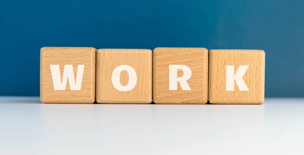 The word WORK on wood cubes. Wooden blocks on blue background. Business and career concept.