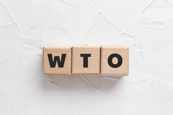 Beyaz desenli macun arkaplanındaki tahta küplere WTO metni. 'Dünya Ticaret Örgütü' nün kısaltması. Kare tahta bloklar. Üst manzara, düz uzanma.