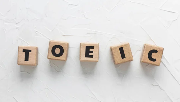 Beyaz desenli macun arkaplanındaki tahta küplere TOEIC metni. Uluslararası İletişim için İngilizce Testi 'nin kısaltması. İngilizce sınavı. Kare tahta bloklar. Üst manzara, düz uzanma.