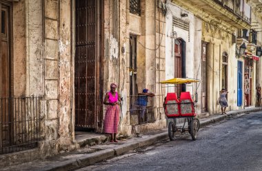 Havana, Küba, Temmuz 2019, Pembe elbiseli bir kadın şehrin en eski bölgesinde bisiklet bekliyor.