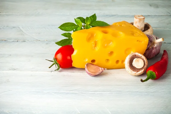 Part cheese with vegetables and basil on wooden board — Stock Photo, Image