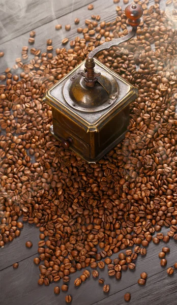 Old vintage coffee grinder on roasted hot beans with smoke — Stock Photo, Image