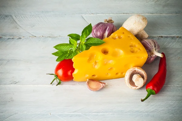 Parte de queijo com legumes e manjericão na placa de madeira — Fotografia de Stock