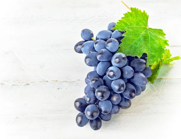 Синий виноград с зелеными листьями на деревянной доске — стоковое фото