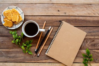 İş için defter planlayıcı sıcak kahve, tatlı aperatifi, çiçekler frangipani düzenleme düz zemin ahşap üzerine yatıyordu