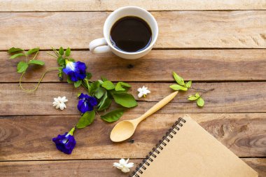 Sıcak kahve, mavi çiçekler, kelebek bezelye düzenleme arka plan tahtasının üzerinde düz bir şekilde yatıyordu.