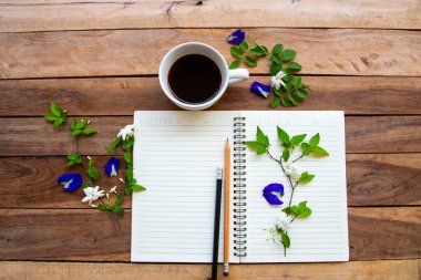 Sıcak kahve, mavi çiçekler, kelebek bezelye düzenleme arka plan tahtasının üzerinde düz bir şekilde yatıyordu.