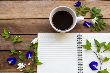 Sıcak kahve, mavi çiçekler, kelebek bezelye düzenleme arka plan tahtasının üzerinde düz bir şekilde yatıyordu.