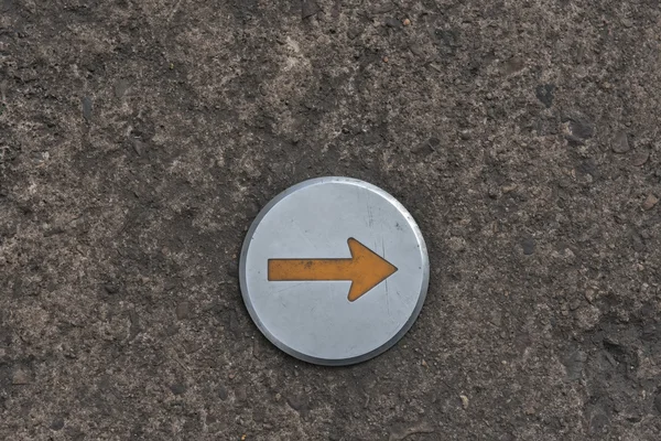 Orange arrow on round metal sign — Stock Photo, Image