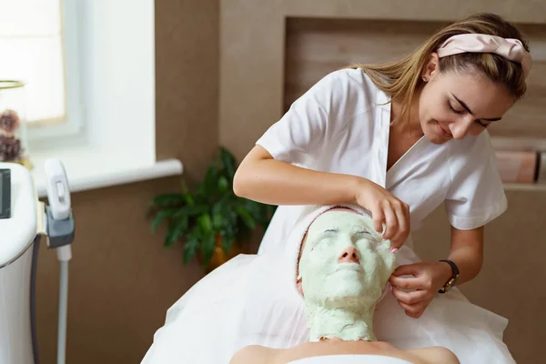 Tapasztalt kozmetikus alginát maszkot távolít el egy kaukázusi nő arcáról. — Stock Fotó