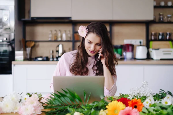 Jonge bloemist op zoek naar laptop en beantwoorden van telefoongesprek — Stockfoto