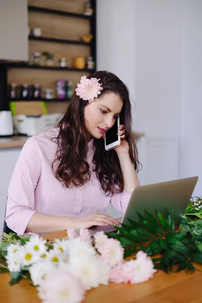 Fiatal virágárus laptopot néz és telefonál. — Stock Fotó