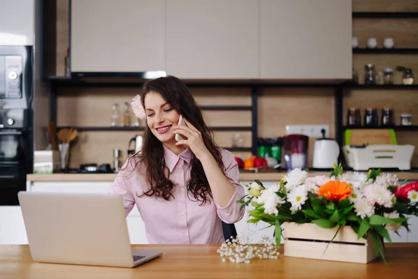 Junge Floristin schaut auf Laptop und nimmt Anruf entgegen — Stockfoto