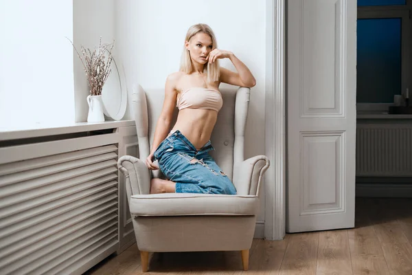 Vrouw in beige beha en blauwe jeans ontspannen op fauteuil — Stockfoto