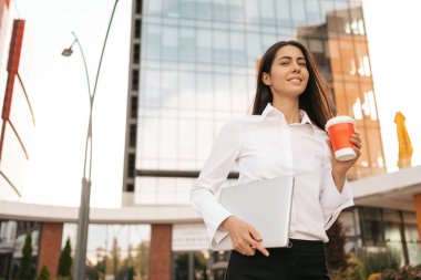 Kurumsal İletişim. Kafkasyalı iş kadını kahvesiyle cep telefonuyla konuşuyor ve iş merkezinin arka planında laptopla yürüyor.