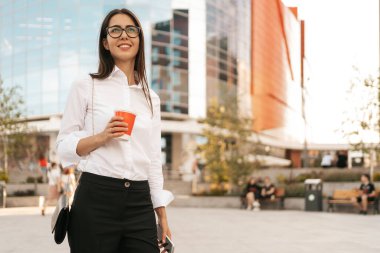 İş kadını işine ara veriyor ve dinleniyor. Bir yandan da iş merkezine gitmek için kahveyle yürüyor..
