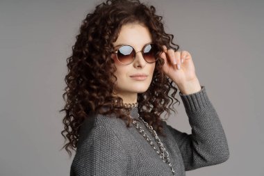 Gri arka planda güneş gözlüklü büyüleyici bir kız..