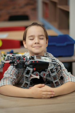 Akıllı okul çocuğu masada oturuyor ve robot bir cihaz yapıyor.