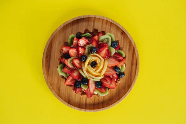 Board with tasty berry cake on yellow background, flat lay — Stock Photo, Image