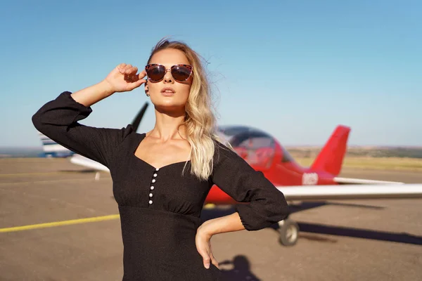 Preciosa dama en gafas de sol posando cerca de avión —  Fotos de Stock