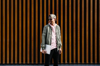 Özgüvenli genç Afro adamın portresi ahşap arka planda dizüstü bilgisayarla poz veriyor.