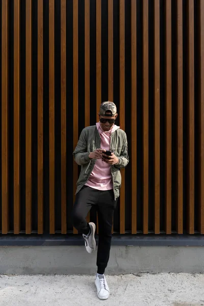 Portret pewnego siebie młodego Afro człowieka pozowanie na drewnianym tle za pomocą telefonu — Zdjęcie stockowe