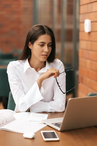 Hermosa mujer en gafas hablando con el ordenador portátil con sonrisa mientras está sentado y trabajando — Foto de Stock