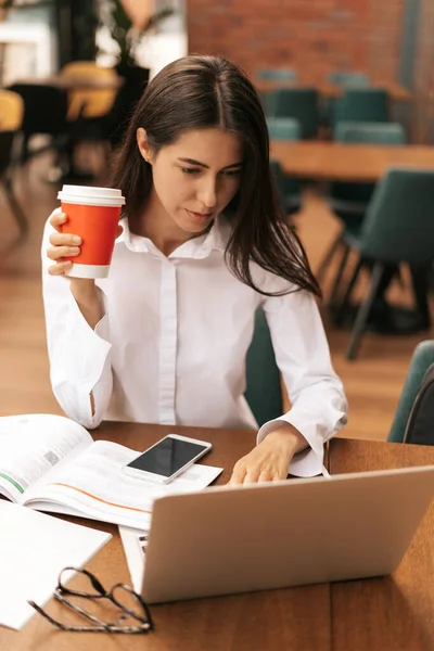 Brunette vrouw drinken koffie te gaan terwijl het werken op laptop — Stockfoto