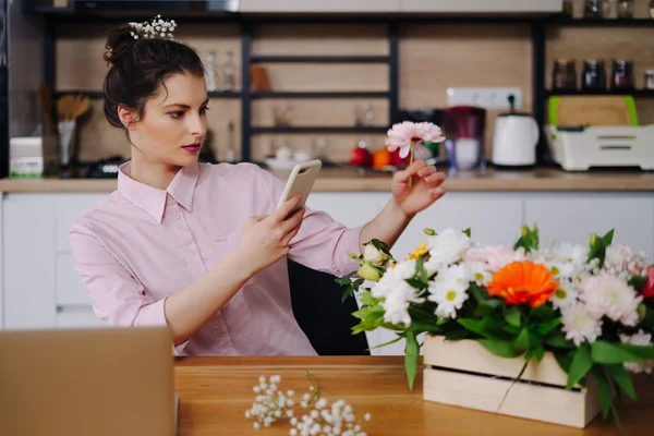 Joven florista mirando a la computadora portátil y respondiendo a la llamada telefónica — Foto de Stock