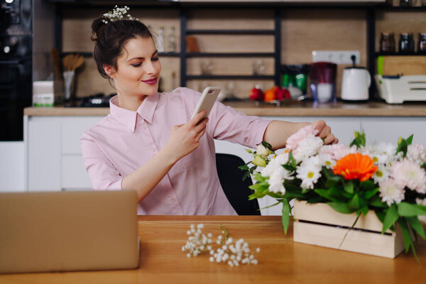 Young florist looking at laptop and answering phone call