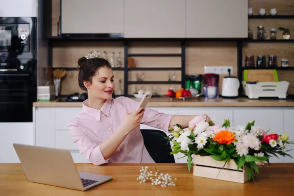 Junge Floristin schaut auf Laptop und nimmt Anruf entgegen — Stockfoto