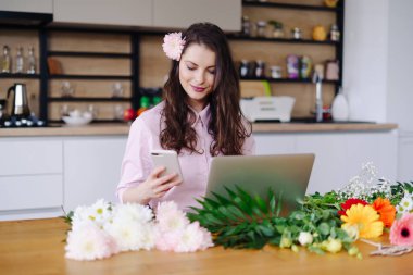Genç çiçekçi dizüstü bilgisayara bakıyor ve telefona cevap veriyor.