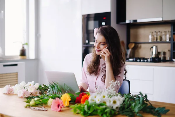 Junge Floristin schaut auf Laptop und nimmt Anruf entgegen — Stockfoto