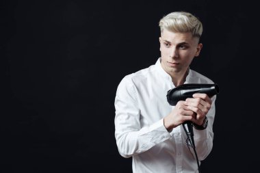 Elinde saç kurutma makinesiyle gülümseyen erkek kuaför.