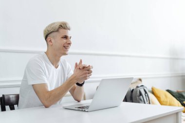 Gülümseyen adam beyaz bir alanda bilgisayar kullanarak çalışıyor.