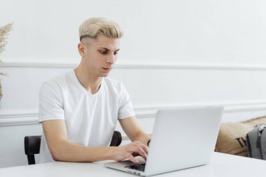 Gülümseyen adam beyaz bir alanda bilgisayar kullanarak çalışıyor.